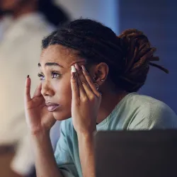 An anxious woman has her fingers pressed up against her temples