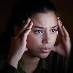  A depressed woman has her fingers on her temples and her thumbs on her lower cheeks while looking sad